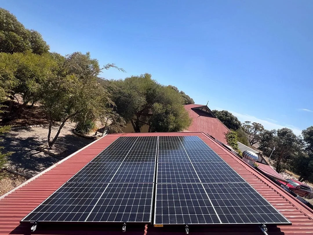 Solar panels on a red steel roof under a clear blue sky